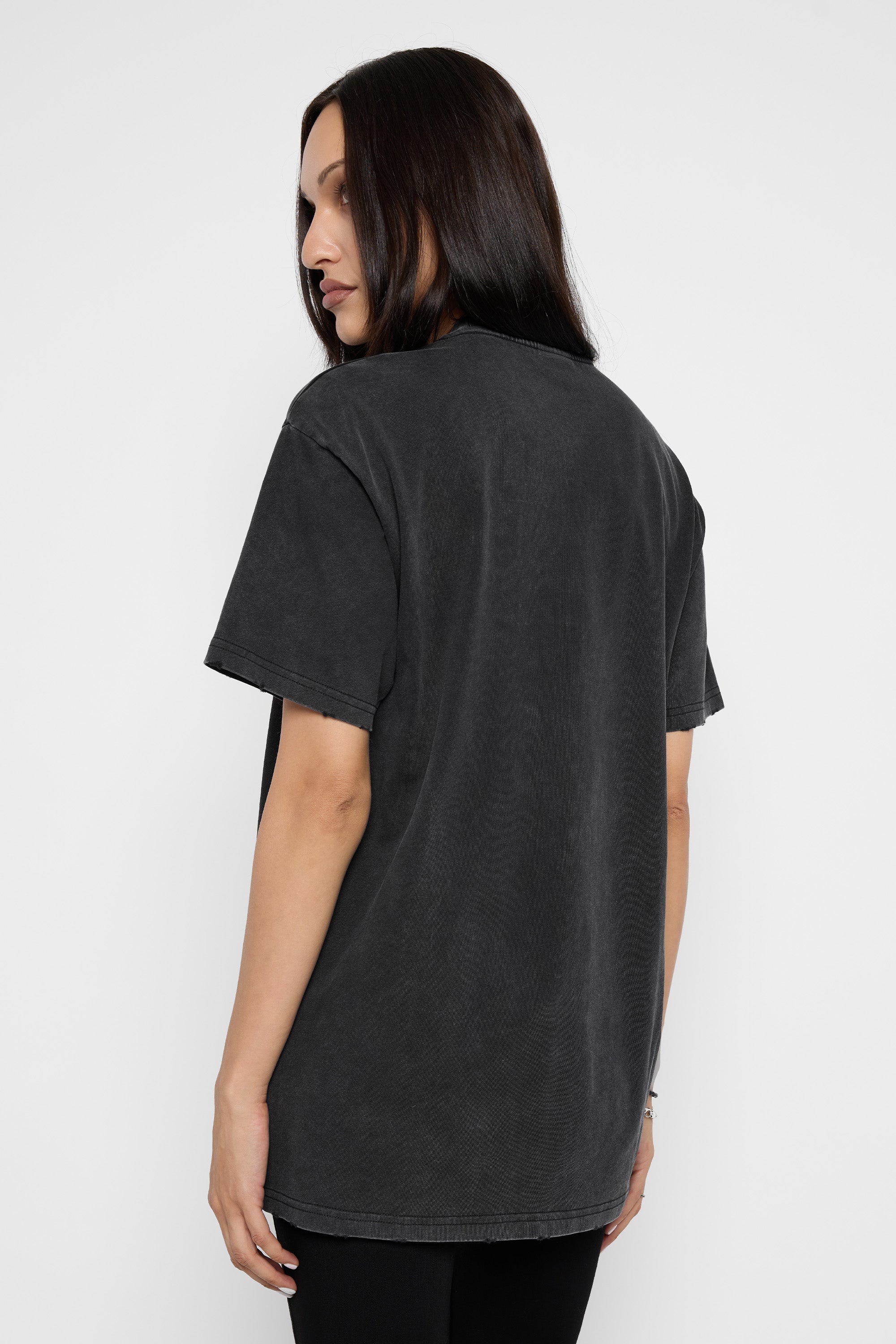 A woman with long dark hair is shown from the back wearing an oversized, washed black t-shirt against a plain light gray background.