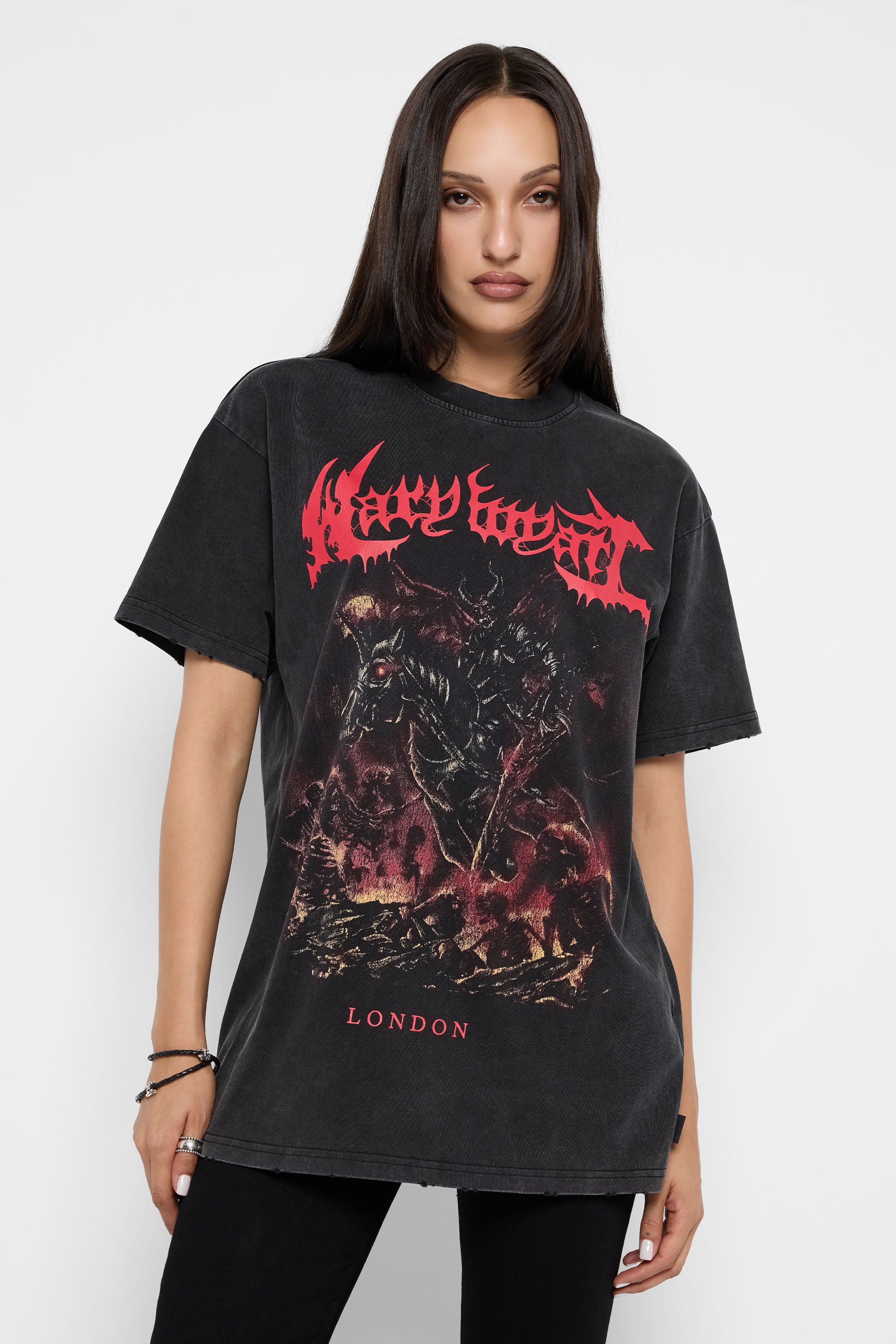 A woman modeling an oversized black acid-wash graphic t-shirt with a red 'Mary Wyatt' band logo and dark fantasy illustration, set against a plain light gray background.