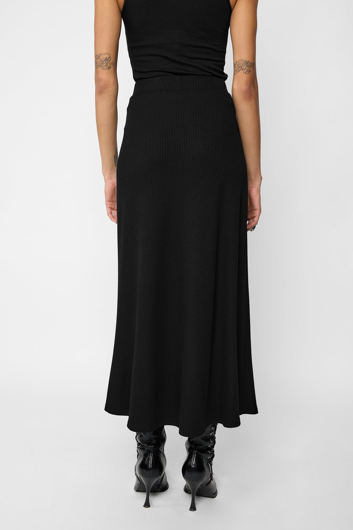 A model from the back wearing the beatriz black midi skirt shot on a light grey studio background.