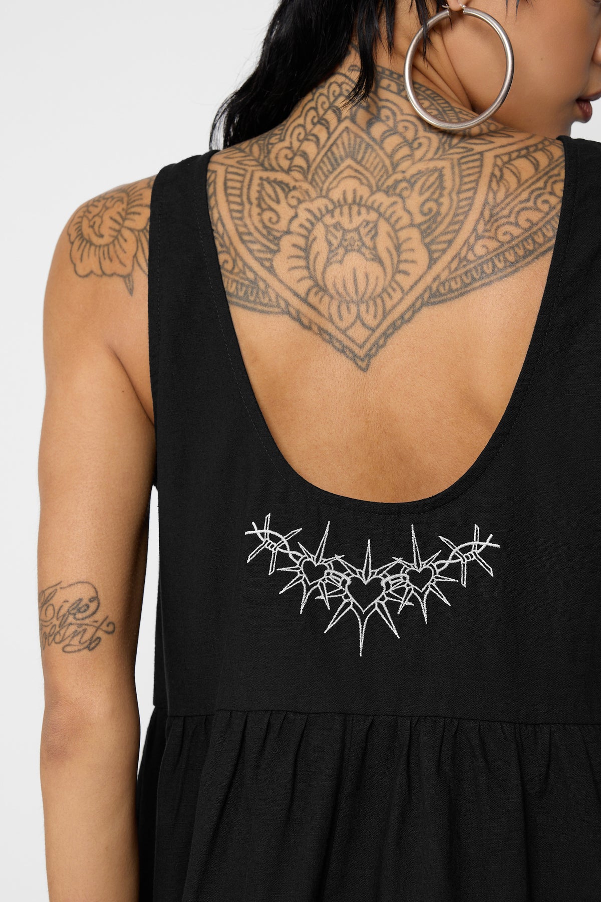 Close-up of the Cora smock dress's scooped back with a white embroidered row of barbed-wire hearts above the gathered waist.